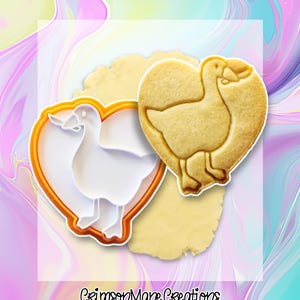 May include: A heart-shaped cookie cutter and a baked cookie, both featuring a goose design. The cookie cutter is white with an orange border. The baked cookie is golden brown and sits on a piece of dough. The text "Crimson Mane Creations" is visible.