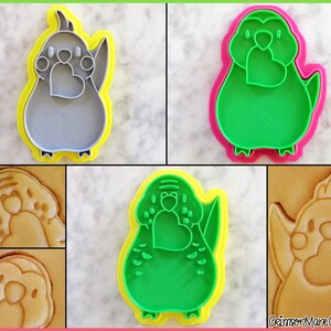 May include: A set of four green and gray cookie cutters shaped like a bird holding a heart. The cutters are shown on a white surface with a cookie made with each cutter.