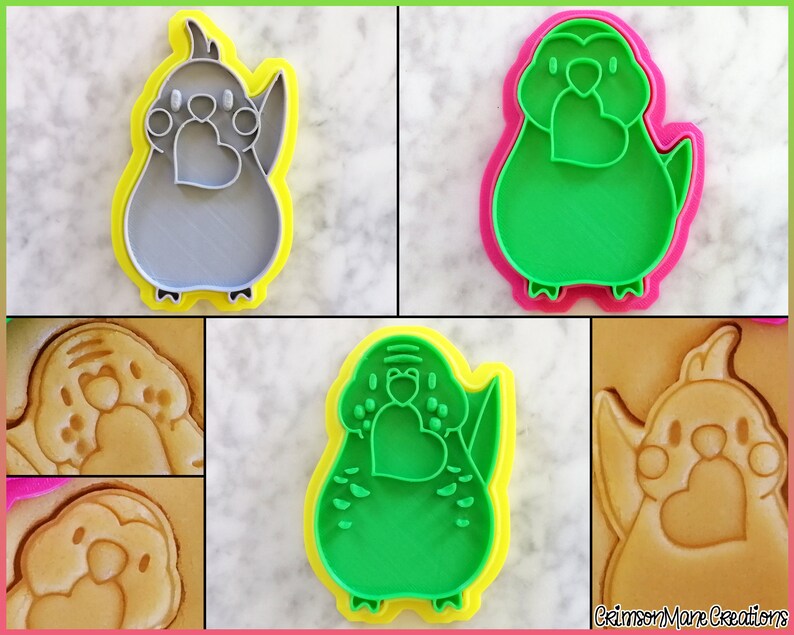 May include: A set of four green and gray cookie cutters shaped like a bird holding a heart. The cutters are shown on a white surface with a cookie made with each cutter.