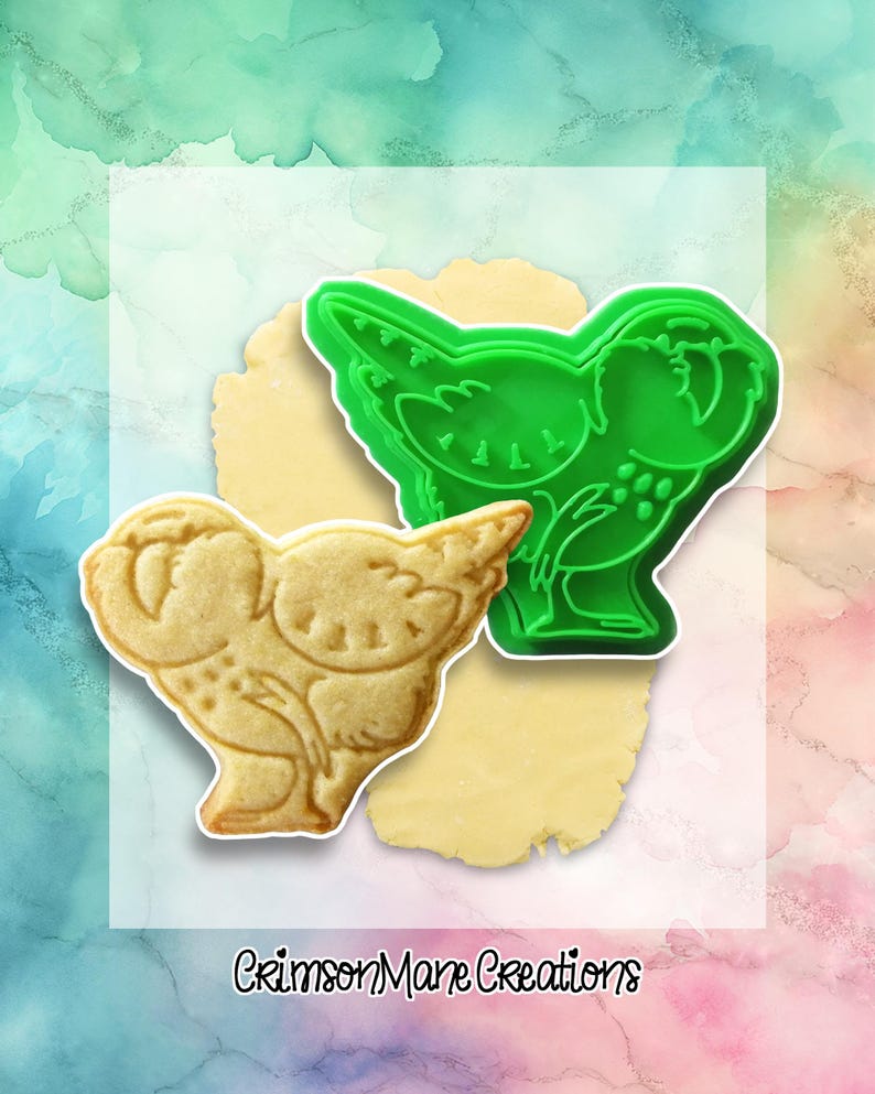 May include: A green plastic cookie cutter in the shape of a bird sits next to a bird-shaped cookie. The cookie is light brown and has detailed markings. The cookie cutter is on a light yellow surface, with a colorful background.