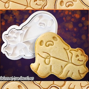 May include: A white plastic cookie cutter in the shape of two ghosts, one larger than the other. The larger ghost is holding the smaller ghost. A baked cookie in the shape of the cookie cutter is shown below.