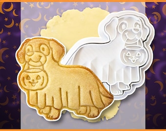May include: A white plastic dog-shaped cookie cutter and a baked golden-brown cookie in the same shape, featuring a dog wearing a ghost costume and holding a jack-o'-lantern bucket. The text CrimsonManeCreations is printed at the bottom.