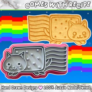 May include: A cat-shaped cookie cutter and a baked cookie are shown. The cookie cutter is gray with a pink outline, and the cookie is golden brown. The cookie has a rectangular body with a cat head and tail. Text at the top says "COMES WITH RECIPE".