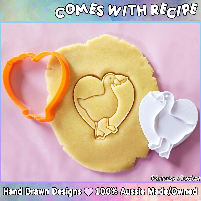 May include: An orange heart-shaped cookie cutter and a white duck-shaped cookie cutter are next to a piece of dough with a duck imprint. The dough is on a pink surface. The text "COMES WITH RECIPE" is at the top.