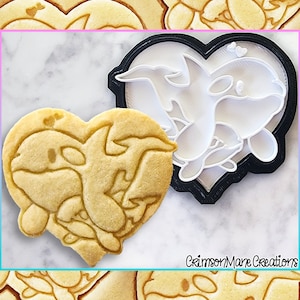 Op de afbeelding: Een hartvormige koekjesvormer en een koekje met een orka-walvisontwerp. De koekjesvormer is zwart en het koekje is lichtbruin. De tekst "Crimson Mare Creations" is zichtbaar in de rechterbenedenhoek van de afbeelding.