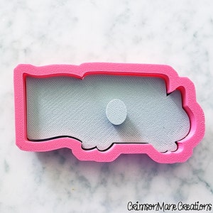 May include: A pink plastic cookie cutter in the shape of a truck. The cutter has a detailed interior and a small circular detail. The background is a light blue color. The words "Crimson Mane Creations" are at the bottom.