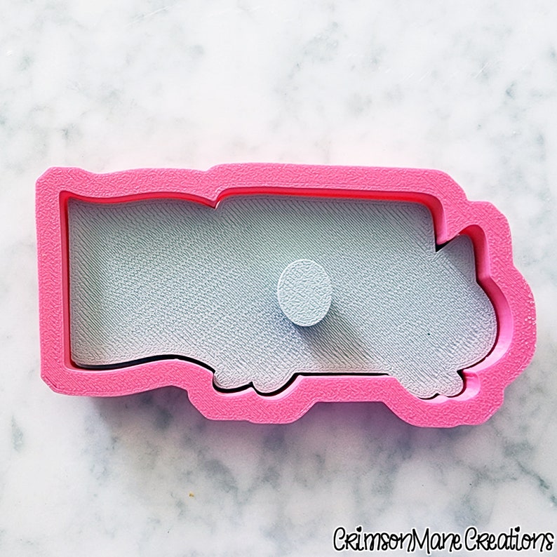 May include: A pink plastic cookie cutter in the shape of a truck. The cutter has a detailed interior and a small circular detail. The background is a light blue color. The words "Crimson Mane Creations" are at the bottom.