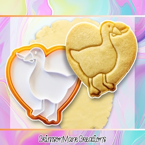 May include: A heart-shaped cookie cutter and a baked cookie, both featuring a goose design. The cookie cutter is white with an orange outline. The baked cookie is golden brown. The text "Crimson Mane Creations" is at the bottom.