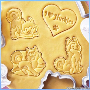 Könnte beinhalten: Nahaufnahme von Keksteig mit geprägten Husky-Hundeformen und einem Herz mit der Aufschrift "I ❤️ Huskies" und einem Pfotenabdruck. Die Ausstecher sind an den Rändern sichtbar. Der Teig hat eine hellbraune Farbe.