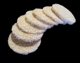 May include: A stack of seven round, white, natural loofah sponges. The sponges are arranged in a semi-circle, with the largest sponge at the top and the smallest sponge at the bottom.