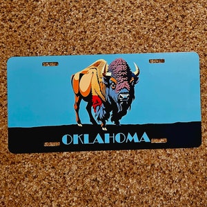 May include: A blue and black metal license plate with a colorful illustration of a bison and the word "OKLAHOMA" in white letters.