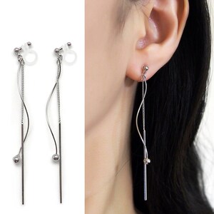 May include: Silver clip-on earrings with a long, dangling chain and a small ball at the end. The chain is twisted and has a straight piece of metal attached to it.