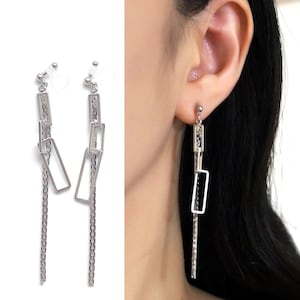 May include: Silver clip-on earrings with a long chain and multiple rectangular links. The earrings are dangling and have a silver finish.