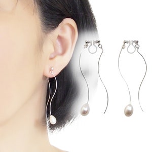 May include: A pair of silver clip-on earrings with a pearl drop. The earrings have a curved wire design.