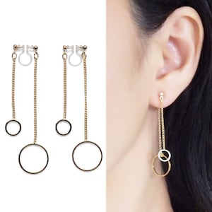 Könnte beinhalten: Goldene Ohrclips mit drei baumelnden Kreisen. Die Ohrringe bestehen aus einer zarten Kette und haben einen kleinen, mittleren und großen Kreis.