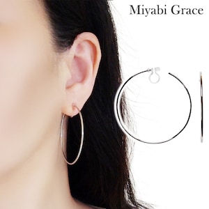 May include: Silver hoop earrings with a clip-on fastening. The earrings are shown on a model's ear.
