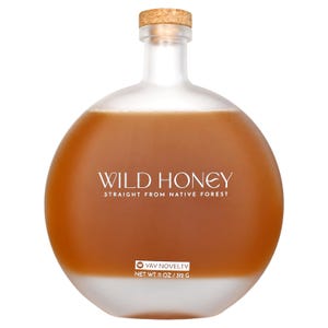May include: A round glass bottle filled with wild honey. The bottle has a cork stopper and a frosted bottom. The text "WILD HONEY STRAIGHT FROM NATIVE FOREST" is printed on the bottle. The net weight is 11 oz / 312 g.