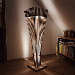 May include: A modern wooden floor lamp with a unique design. The lamp features vertical wooden slats that create a warm, ambient light. The base is square, and the lamp stands tall, adding a stylish touch to any room. The lamp is approximately 60 inches tall.