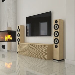 Op de afbeelding: Een moderne woonkamer met een flatscreen-tv die aan de muur is gemonteerd boven een houten entertainmentcenter. Twee hoge luidsprekers staan aan weerszijden van het entertainmentcenter. Een open haard is zichtbaar op de achtergrond.