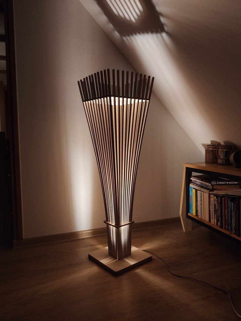 May include: A modern wooden floor lamp with a unique design. The lamp features vertical wooden slats that create a warm, ambient light. The base is square, and the lamp stands tall, adding a stylish touch to any room. The lamp is approximately 60 inches tall.