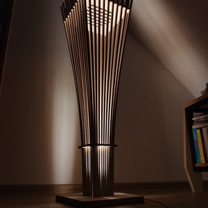 May include: A modern, wooden floor lamp with a unique design. The lamp features a square base, a rectangular midsection, and a flared top, all constructed with vertical wooden slats. The lamp emits a warm, inviting glow, creating a cozy ambiance.