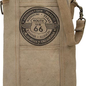 May include: A tan canvas crossbody bag featuring a Route 66 graphic. The bag has a front pocket, a long adjustable strap, and a top zipper closure. The Route 66 graphic is in a circular design with the words "Arizona, New Mexico, Texas, Kansas, Illinois, Oklahoma, California, Missouri" around the edge.