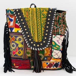 May include: A colorful patchwork backpack with black leather accents and fringe. The backpack is made of various fabrics with embroidered designs in shades of red, green, yellow, blue, and white.