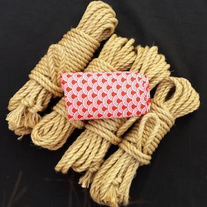 K&ouml;nnte beinhalten: Ein Satz aus f&uuml;nf nat&uuml;rlichen Jute-Seilen, die jeweils aufgerollt und zusammengebunden sind. Die Seile sind kreisf&ouml;rmig angeordnet, mit einem roten und wei&szlig;en Stoffquadrat mit Muster in der Mitte.