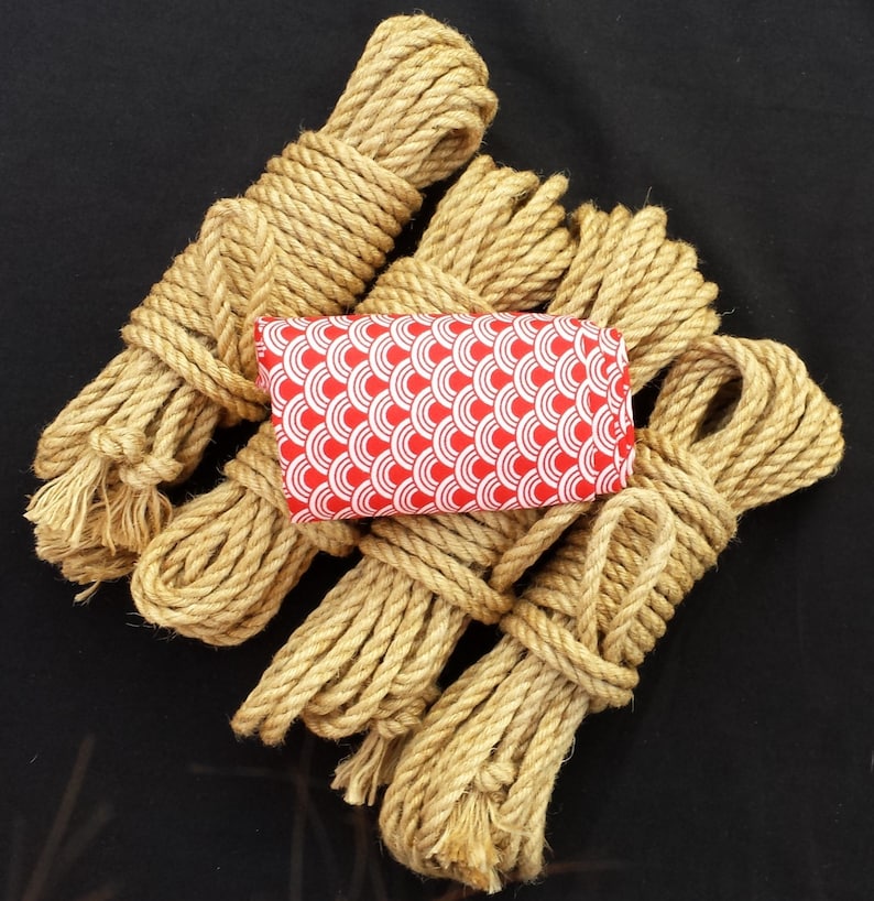 K&ouml;nnte beinhalten: Ein Satz aus f&uuml;nf nat&uuml;rlichen Jute-Seilen, die jeweils aufgerollt und zusammengebunden sind. Die Seile sind kreisf&ouml;rmig angeordnet, mit einem roten und wei&szlig;en Stoffquadrat mit Muster in der Mitte.
