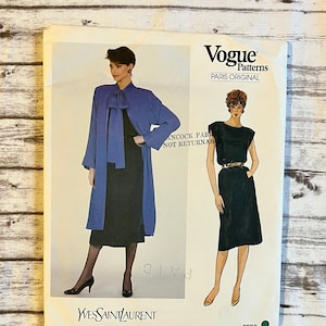 May include: A vintage Vogue Patterns sewing pattern for a dress and coat by Yves Saint Laurent. The pattern number is 2990. The pattern features two models wearing the designs. The model on the left is wearing a blue coat with a large bow at the neck and a black dress. The model on the right is wearing a black sleeveless dress with a gold belt.