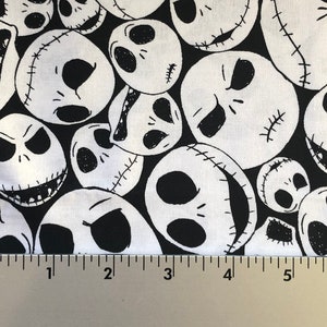 May include: Black and white fabric with a repeating pattern of Jack Skellington's face from the Nightmare Before Christmas. The fabric is shown against a ruler.
