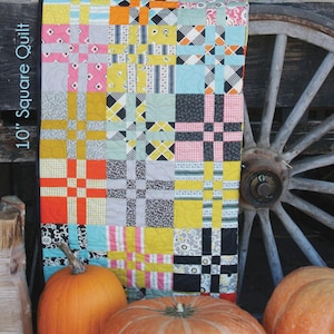 May include: A colorful patchwork quilt with the name "Katie" in large letters. The quilt is made of squares in various colors and patterns, including pink, yellow, and black. The quilt measures 48 inches by 56 inches.