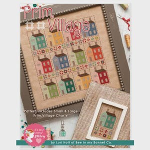 May include: A framed cross-stitch sampler titled "Prim Village" featuring a grid of colorful houses. The houses are in shades of blue, green, yellow, and red. The text "Pattern includes Small & Large Prim Village Charts!" is visible.