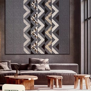 May include: A square quilt featuring a vertical central panel of repeating chevron patterns in shades of charcoal, black, white, and tan, flanked by solid gray sections with a subtle quilted texture. The text reads ZEN CHIC SHADOW PATH.