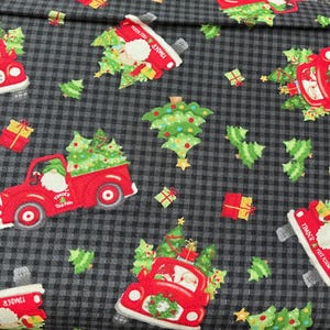 May include: A fabric with a repeating pattern of red trucks carrying Christmas trees and gifts, set against a gray and black checkered background. The trucks have the text "Timber Tree Farm". Green Christmas trees and small gifts are scattered throughout the design.