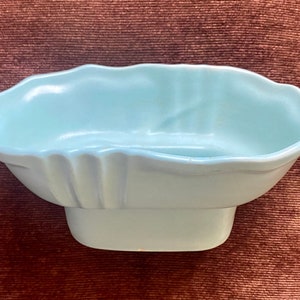 May include: A light blue ceramic dish with a scalloped rim and a rectangular base. The dish has a smooth, glossy finish and is likely used for decorative purposes or serving small items.