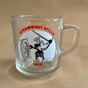 May include: A clear glass mug with a handle. The mug has a black and white image of Mickey Mouse as Steamboat Willie with the text "Steamboat Willie 1928" and a Disney copyright symbol.