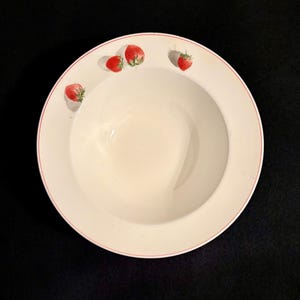 May include: White ceramic bowl with a red rim and four strawberry illustrations. The strawberries are red with green stems and leaves. The bowl is round and has a deep center.
