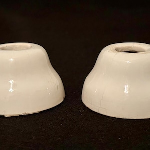 May include: Two white ceramic light fixture bases with a glossy finish. The bases have a flared, bell-like shape with a circular opening at the top. The bases are on a dark surface.