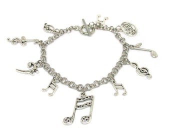 Puede incluir: Un brazalete de plata con dijes de notas musicales, incluyendo una clave de sol, una clave de fa y un pentagrama. El brazalete tiene un cierre de plata.