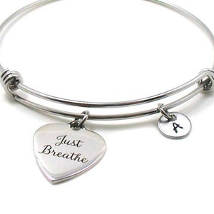 May include: Silver expandable bangle bracelet with a heart charm engraved with the words "Just Breathe" and a round charm with the letter "A".