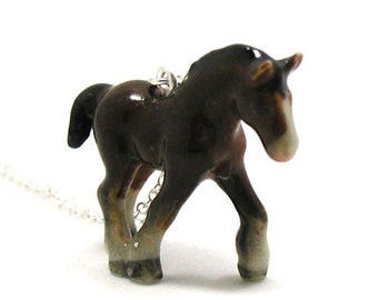 May include: A brown and white porcelain horse figurine necklace. The horse is standing on all four legs and has a silver chain.