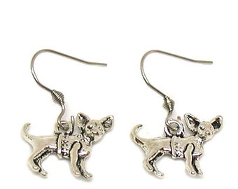 May include: A pair of silver dangle earrings featuring a small dog charm. The dog is wearing a backpack and has a playful expression.