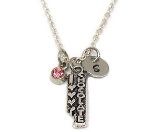 May include: Silver necklace with a charm that says "I love chocolate" and a pink crystal charm. The necklace also has a silver charm with the letter "G" on it.