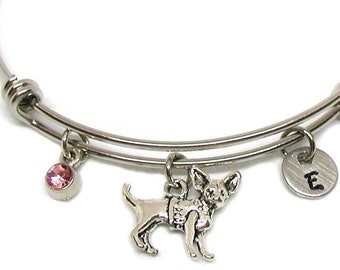 May include: A silver expandable bangle bracelet with a pink crystal charm, a silver charm of a chihuahua, and a silver charm with the letter "E" engraved on it.