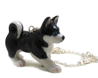 May include: A black and white porcelain husky puppy charm on a silver chain necklace. The puppy is standing on all fours and looking to the right.