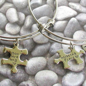 May include: Two silver bangle bracelets with puzzle piece charms. One charm says "You are my" and the other says "missing piece".