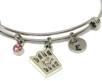 Puede incluir: Un brazalete expandible de plata con tres dijes: un cristal rosa, un dije con las palabras "Pink Corn" y un dije con la letra "E".
