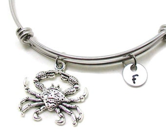 May include: Silver expandable bangle bracelet with a silver crab charm and a silver charm with the letter "F" hanging from it.