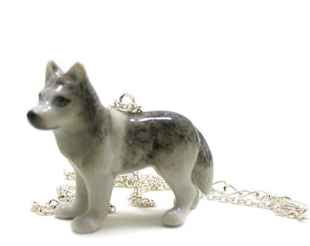 May include: A silver chain necklace with a porcelain wolf pendant. The wolf is gray and white with black markings.
